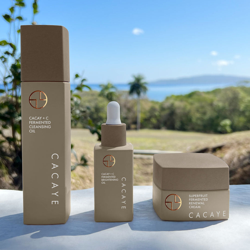 
                  
                    CACAYE CaCay + Fermented Skincare Trio Holiday Set with green tropical plants and blue sky and ocean
                  
                